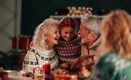 Grandparents and grandchild laughing while sitting at table engaging in healthy holiday eating