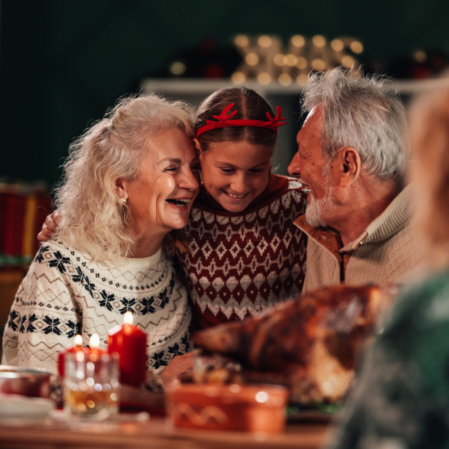 Grandparents and grandchild laughing while sitting at table engaging in healthy holiday eating