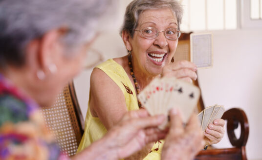 Adult day care benefits seniors by providing socialization opportunities, like these two senior women enjoying a game of cards.