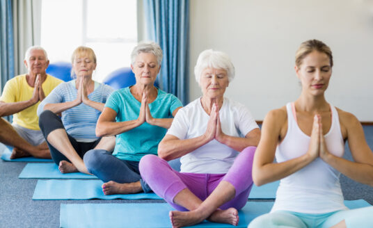 A group of seniors practicing yoga. The benefits of yoga for seniors range from improved health, reduced stress, and making new friends.