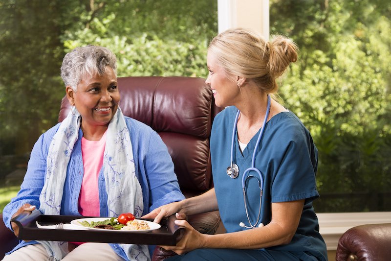 A senior woman speaks to her home health care nurse. As a senior ages, they may find themselves deciding between in-home senior care and assisted living. There are benefits to both, depending on the senior's needs.