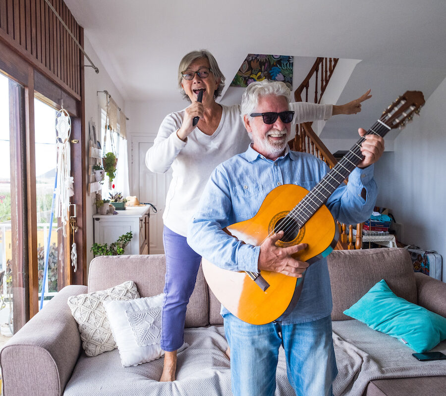 Two older adults having fun while singing and playing the guitar indoors.