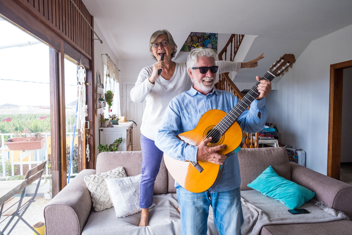 Two older adults having fun while singing and playing the guitar indoors.
