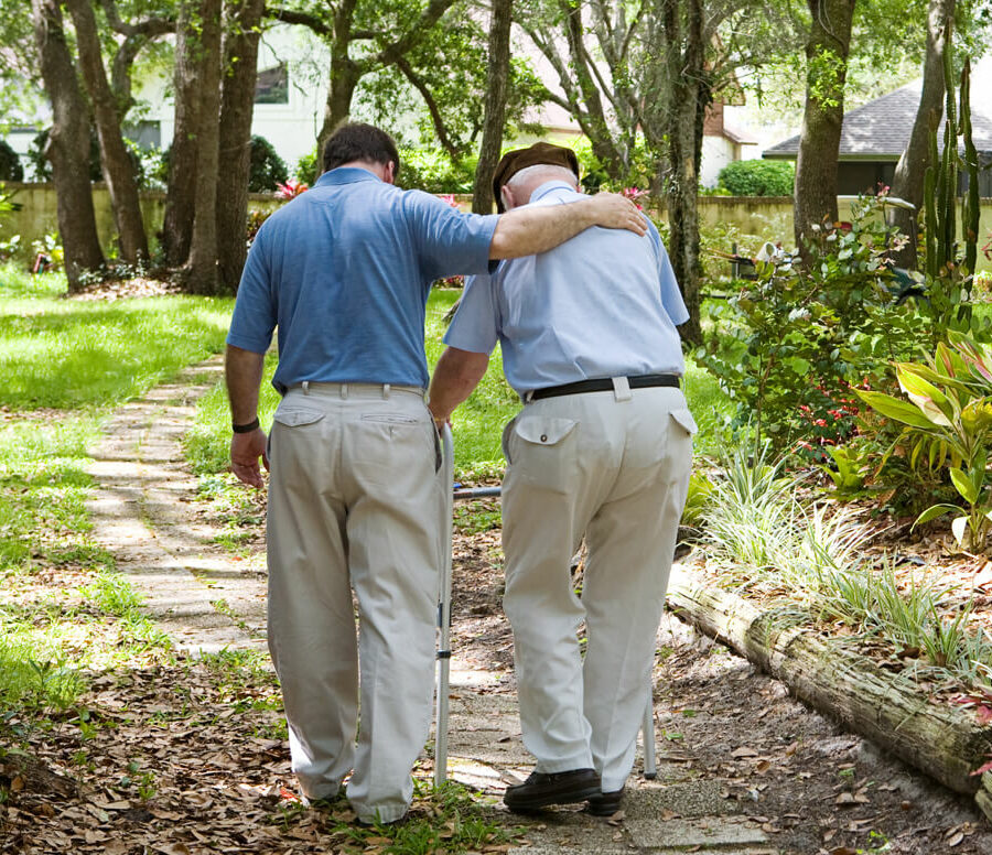 A an adult son walks with his father down a path. There are many sacrifices family caregivers make to ensure that their loved ones receive the care they need—including finances and personal well-being.