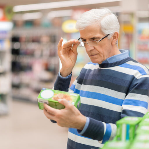 A senior man in a grocery store reads a nutrition label. Getting the most nutritious foods, with fewer calories, is an important part of weight loss for seniors.