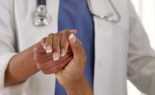 A doctor holds a patient's hand and practices age-friendly health care