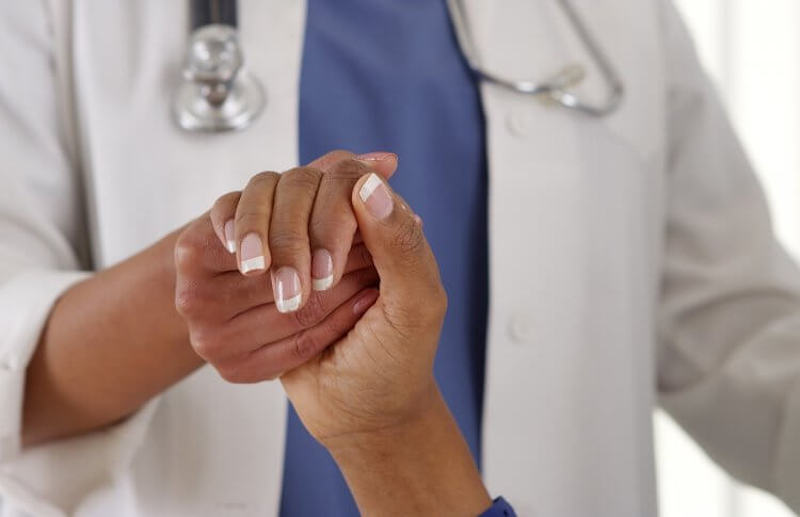 A doctor holds a patient's hand and practices age-friendly health care