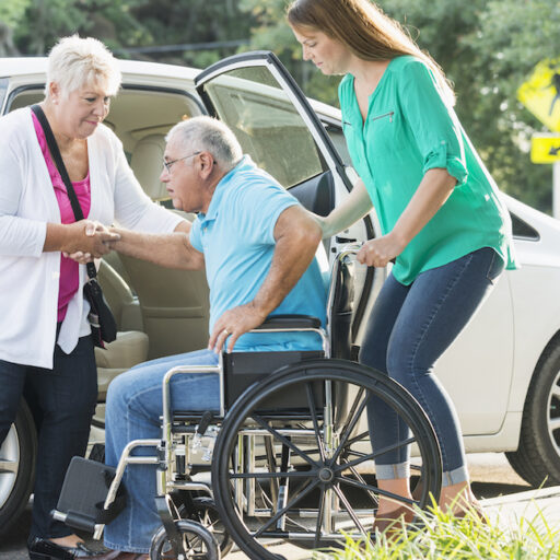 A wife and daughter help a senior man with differing care needs get into a car