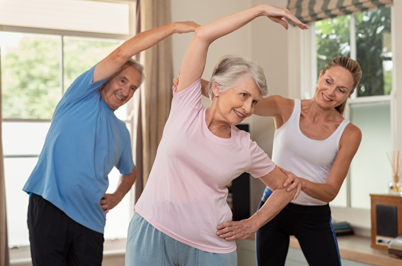 Exercise is just one way of improving quality of life for seniors. Here, a senior man and senior woman work with a trainer in an exercise class.