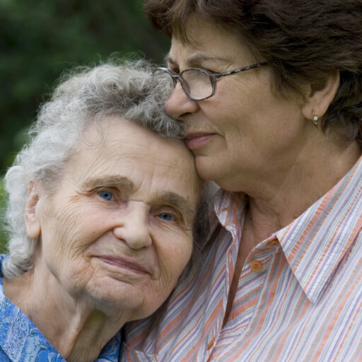 An older adult woman hugs her senior mother.