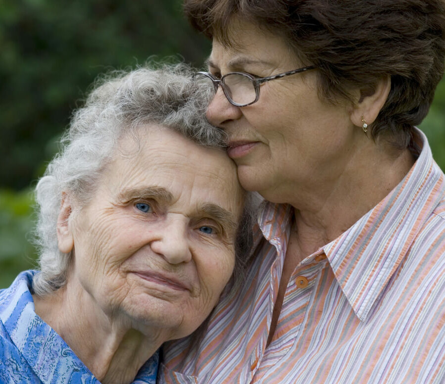 An older adult woman hugs her senior mother.