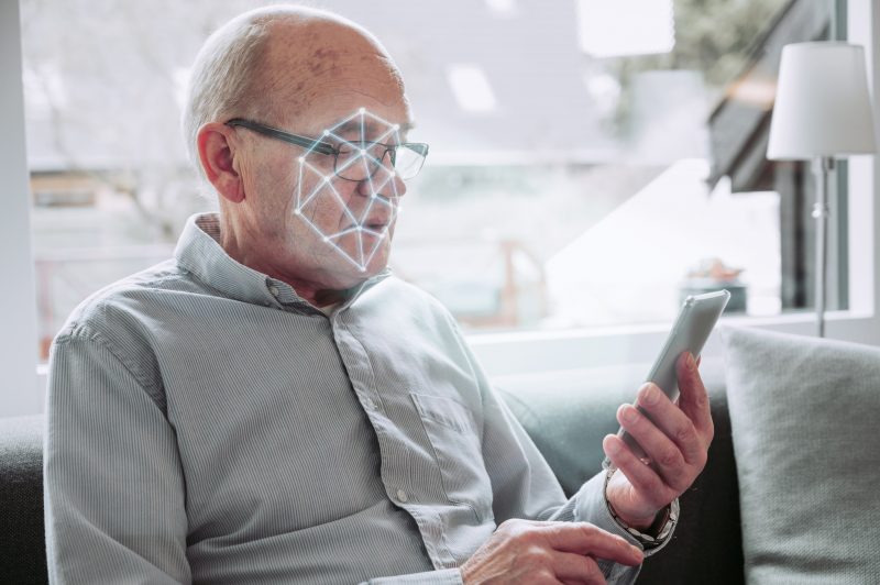 There is a lot of research about AI and aging happening now. Here, a man holds up his smart phone as it scans his face.