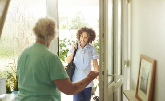 A caregiver meets a senior woman at her front door for in-home respite care services.