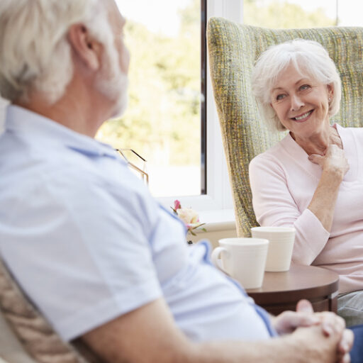 A senior couple living in a retirement community sits and chats in their personal apartment.