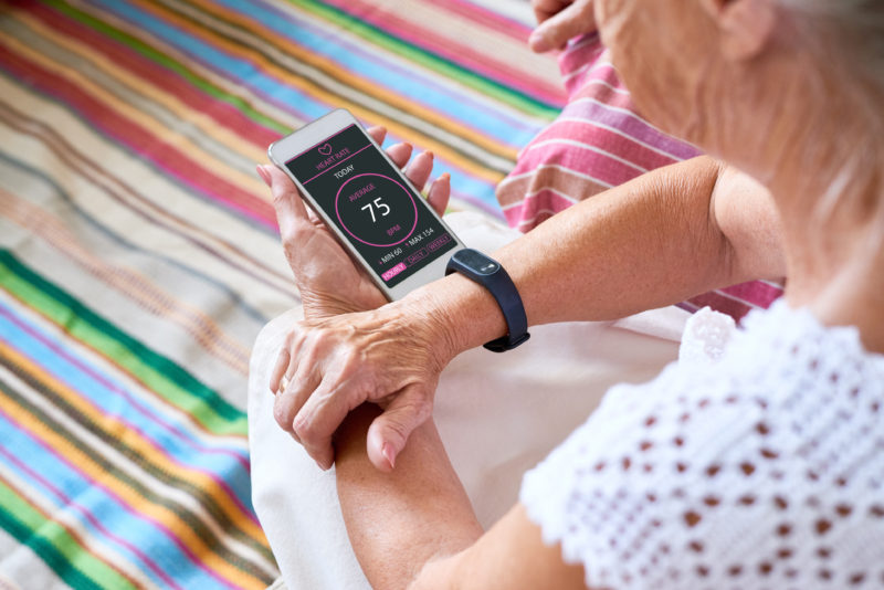 Technology improves quality of life for seniors. Here, a senior woman reviews her heart rate on her smart phone, which is connected to a Fitbit.