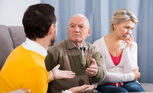An adult man talks with his senior father and mother about aging. Talking to your parents about aging can be a difficult conversation, as pictured here.