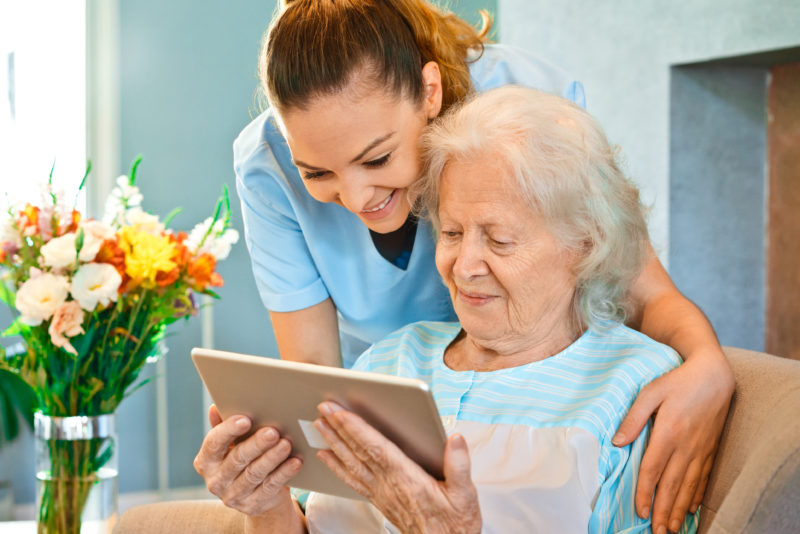 Respite care worker helps elderly woman use a tablet.