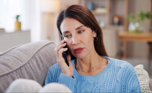 Adult woman remote caregiving and looking concerned while talking on phone