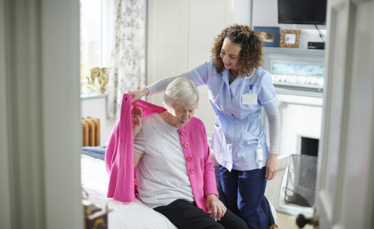 A professional caregiver helps a senior woman with Activities of Daily Living (ADLs).