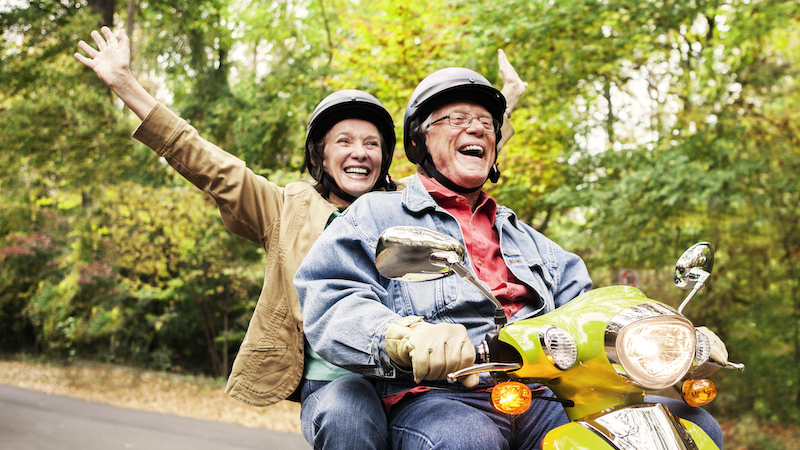 A happy senior couple riding a scooter as a way to enjoy healthy senior activities