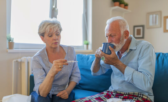 A senior woman takes her husband's temperature, watching for pneumonia symptoms.