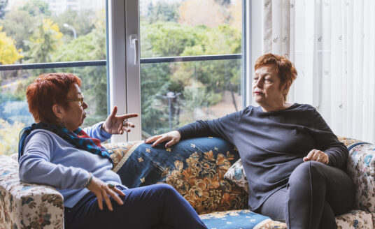 Adult child caring for an aging parent by sitting and having a discussion with her senior aged mother on a couch