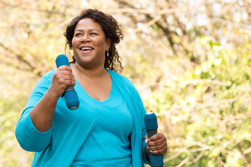 African American woman walking with weights for heart health and smiling.