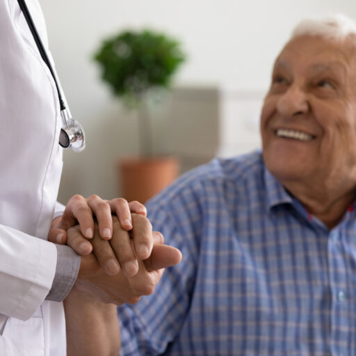 Senior man holding hand of doctor at annual checkup for seniors