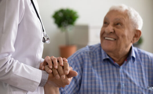 Senior man holding hand of doctor at annual checkup for seniors