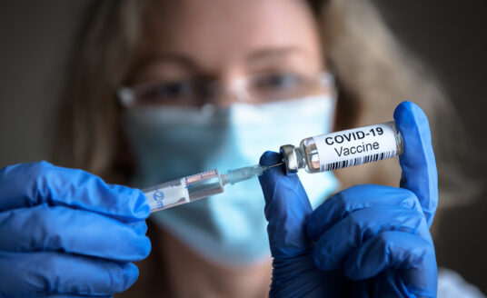 Female doctor holds syringe and bottle with COVID-19 vaccine intended for use in a senior
