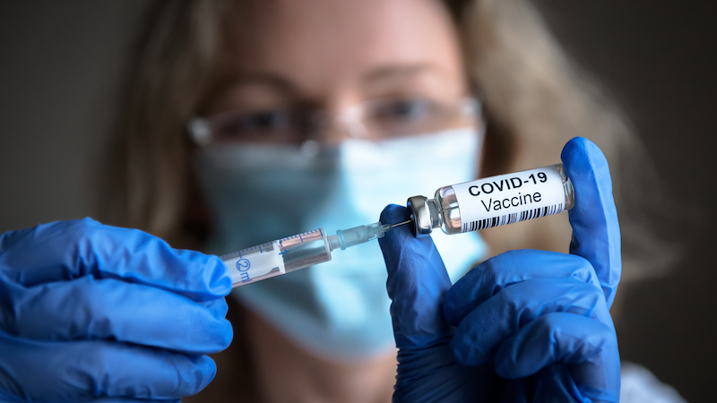 Female doctor holds syringe and bottle with COVID-19 vaccine intended for use in a senior