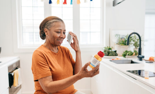 Senior woman on the phone looking at a prescription medication, practicing proper medication safety for seniors