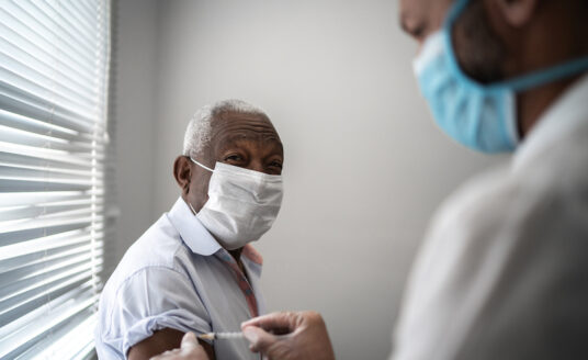 Nurse applying COVID-19 vaccine on elderly patient's arm wearing face mask