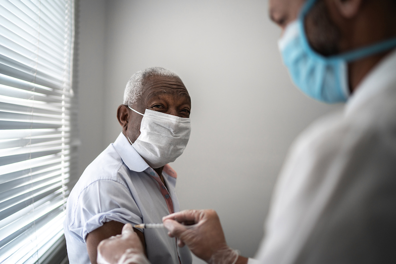 Nurse applying COVID-19 vaccine on elderly patient's arm wearing face mask
