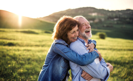 Side view of senior couple in golden years hugging outside in spring nature at sunset.