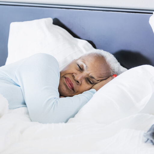 A senior African-American woman sleeping in bed to practice self-care, lying on her side.