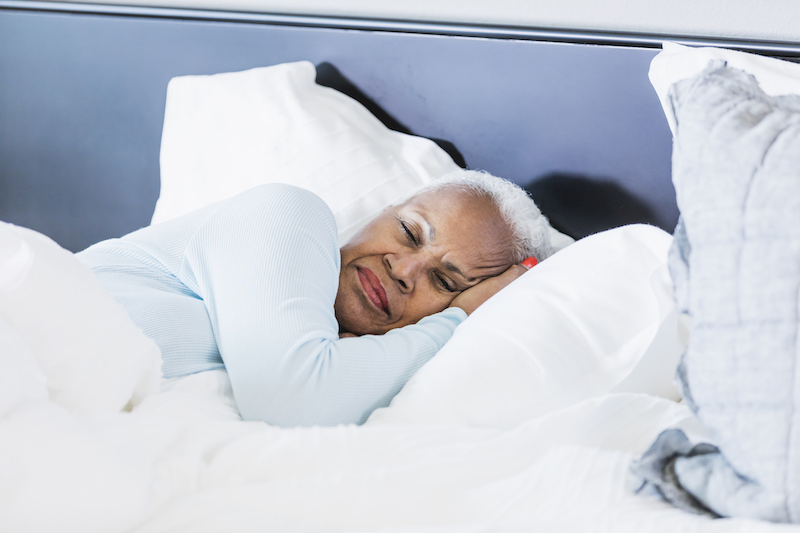 A senior African-American woman sleeping in bed to practice self-care, lying on her side.