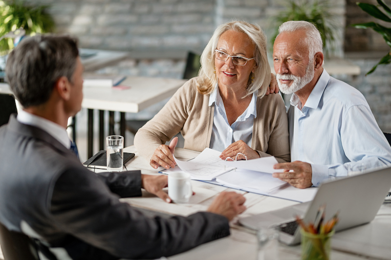 Happy senior couple talking with elder law attorney while analyzing documents on a meeting in the office.