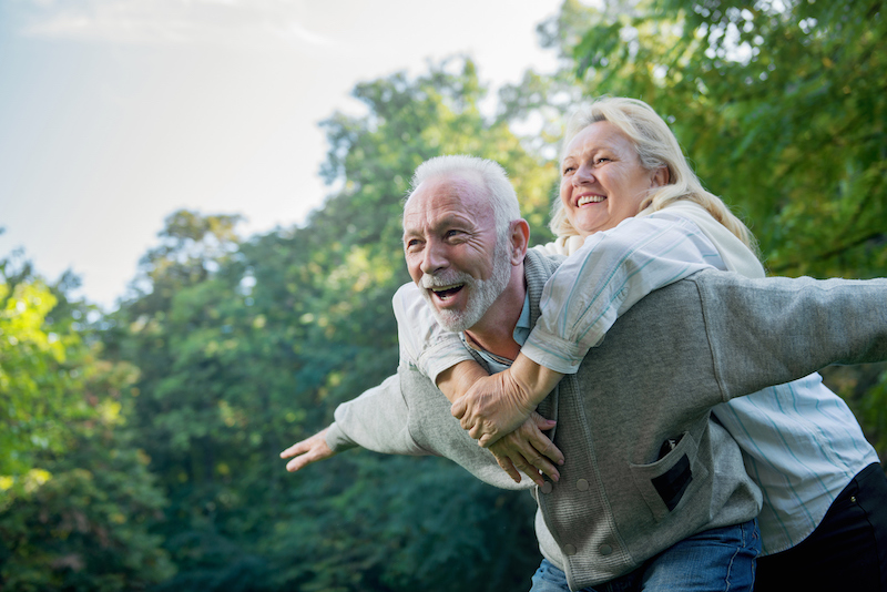 Happy, healthy senior couple smiling outdoors in nature with spring foliage | active senior living