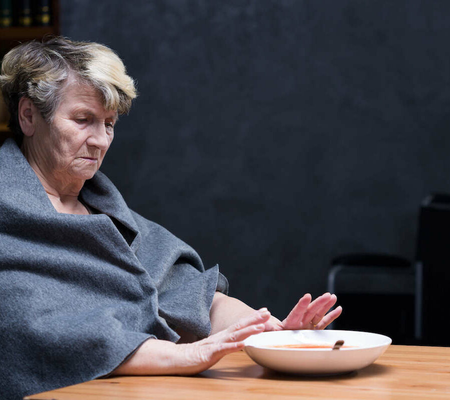 An elderly woman sitting at a table alone and pushing away her dinner plate.