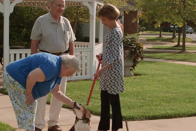 A senior man and woman stop to admire another senior woman's dog