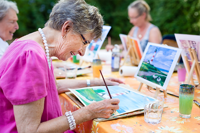 Senior women laugh and paint outdoors at The Oaks at Bethesda