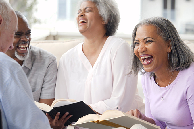 Four seniors - two men and two women - laugh over a book in book club