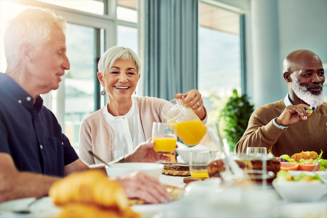 Two senior men and a senior woman enjoy breakfast with orange juice and fruit