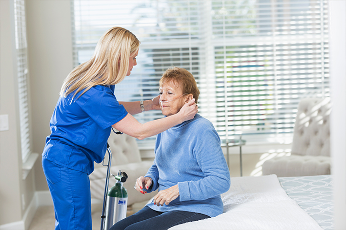 A female nurse or doctor in blue scrubs checks the ears of an assisted living patient