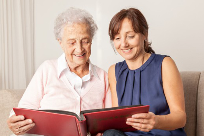 A young woman with brown hair and an older white woman in a pink shirt look at a photo book together in a St. Louis nursing home