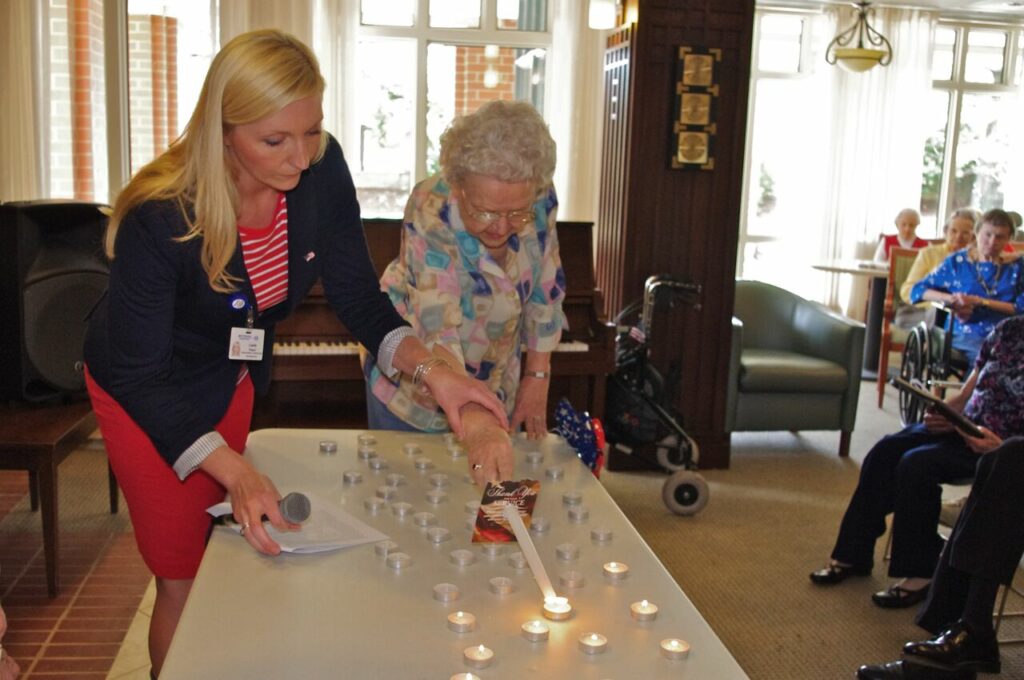 Leslie Schaeffer, hospice veteran liaison, assists a Bethesda Orchard resident in lighting a candle for her deceased husband, a WWII veteran, on Memorial Day.