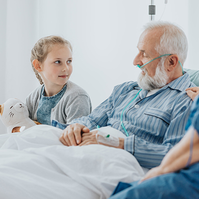 A senior man receiving hospice care talks to his granddaughter who is sitting bedside