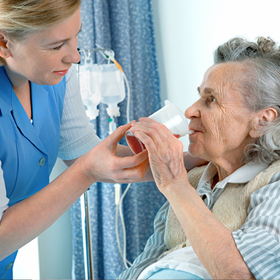 A senior woman receives hospice care as a young female nurse helps her drink fluids