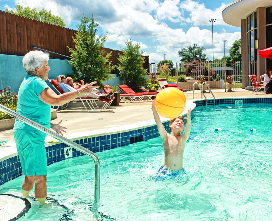 A senior woman and her grandchild in a large outdoor pool playing with a beach ball